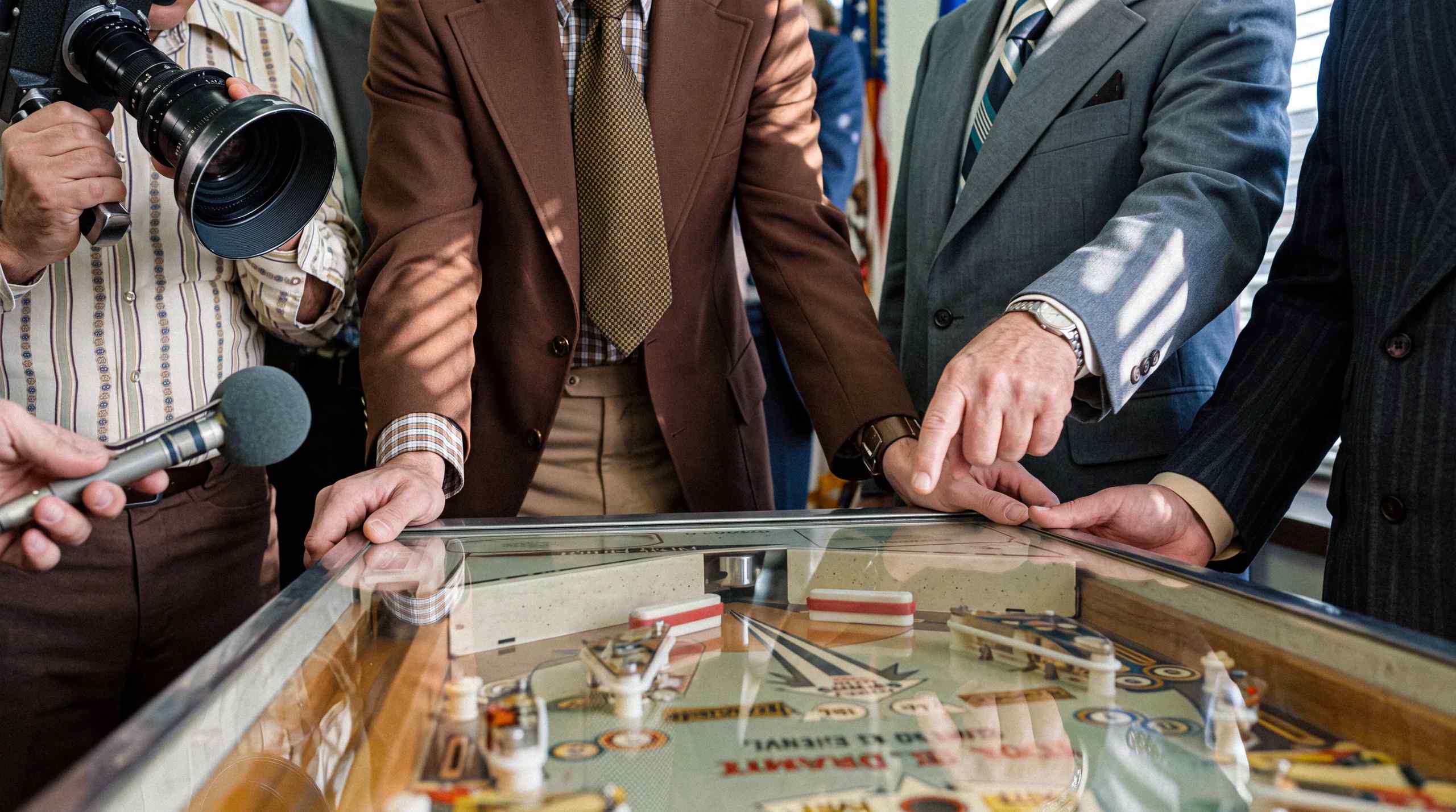 A pinball presentation with men in suits playing on the machine.